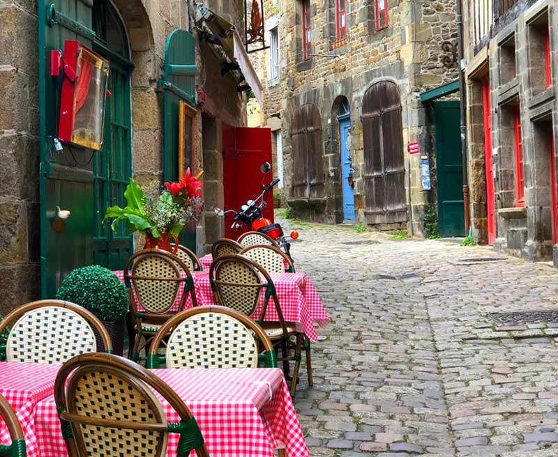 Tables couvertes de chiffons à carreaux rouges et blancs à l'extérieur d'un restaurant dans une rue pavée de Dinan