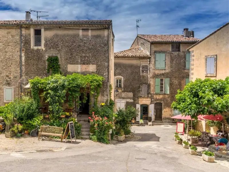 Vieilles maisons en pierre aux volets sur une petite place, un restaurant aux parasols rouges, sud de la France