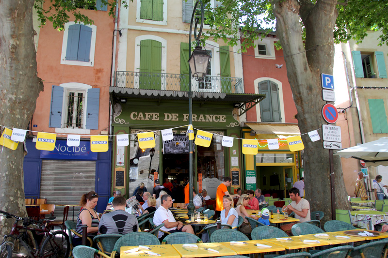 Des gens assis à l'extérieur d'un café en France, des platanes donnent de l'ombre