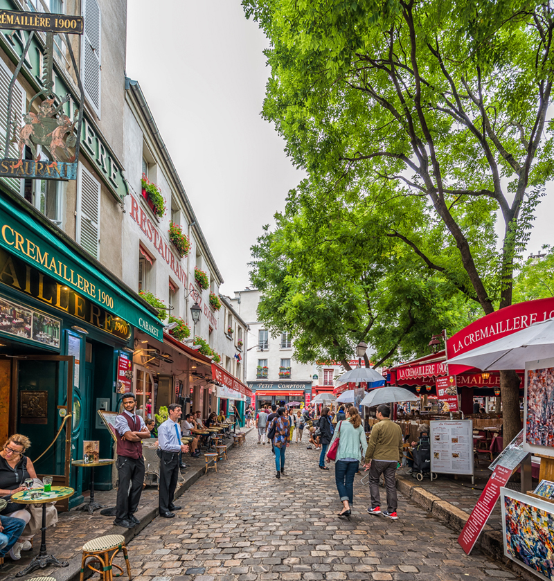 Rue pavée de Montmartre Paris, bordée de boutiques et de bars colorés, des arbres feuillus surplombent les rues