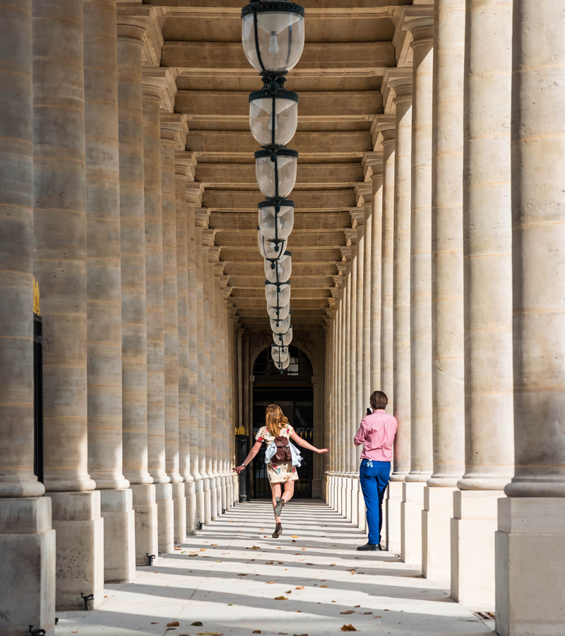 Une femme saute le long d'une rue à arcades à Paris, des lampes au-dessus pendant qu'un homme prend une photo