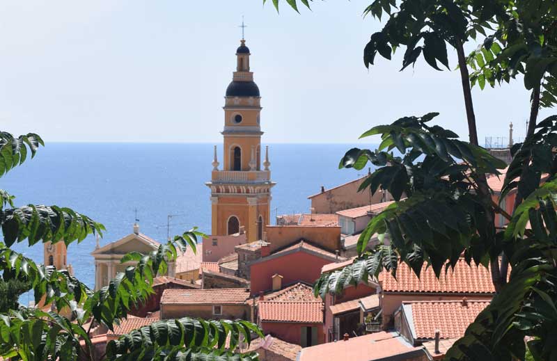 Tour de l'église pointue atteignant au-dessus des toits en terre cuite, mer Méditerranée en arrière-plan à Menton, France