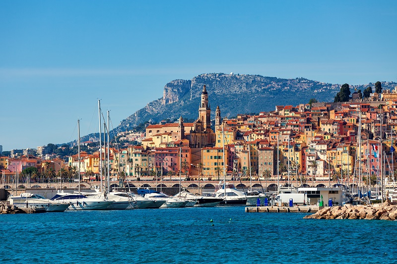 Littoral de Menton bordé de maisons couleur citron contre un ciel ensoleillé et une mer Méditerranée calme